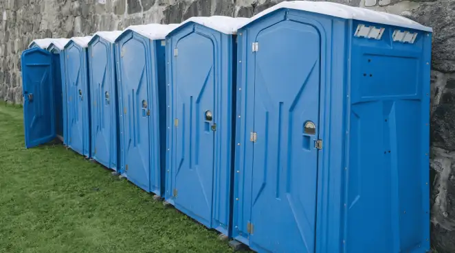 Row of blue portable toilets lined up on grass against a stone wall for event sanitation in Bloomington, IN