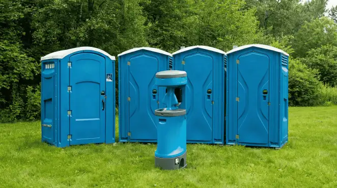 Four blue portable toilets and a matching hand washing station on grass near trees, a common sight at local outdoor events in Bloomington, IN