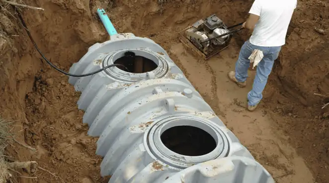 Septic tank installation showing a technician compacting soil around a new poly septic tank in an excavation pit in Bloomington, IN